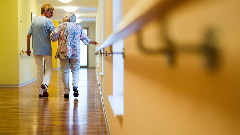 Eine Pflegekraft geht in einem Pflegeheim mit einer älteren Dame über einen Korridor. Derzeit sind es oft Leiharbeiter, die sich um die Patienten kümmern.