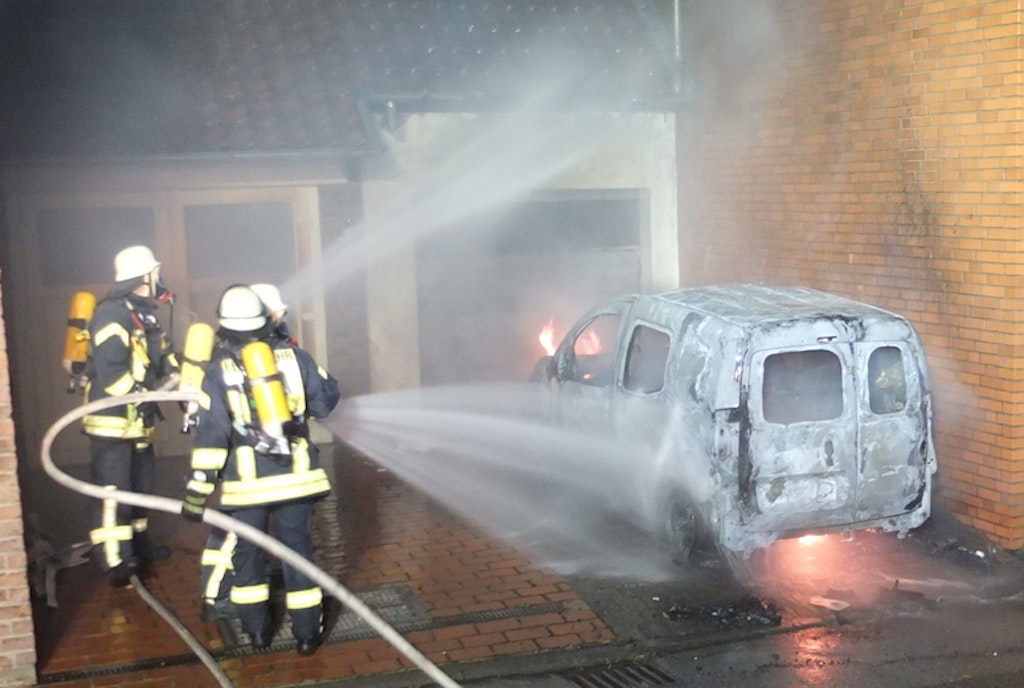 Feuerwehrleute löschen ein brennendes E-Auto, das während des Ladevorgangs in Brand geraten ist.