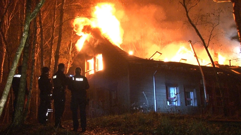 Polizisten stehen vor dem brennenden Haus.