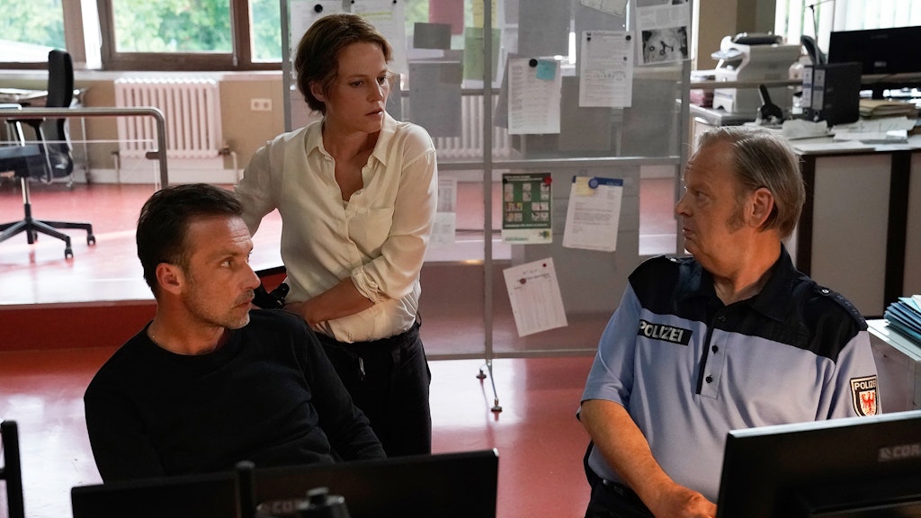 Polizeihauptmeister Wolfgang Neumann (Fritz Roth, r.) zeigt Kriminalhauptkommissarin Olga Lenski (Maria Simon) und Kriminalhauptkommissar Adam Raczek (Lucas Gregorowicz, l.) neue Beweismittel im Zusammenhang mit dem Mord an der jungen Journalistin.