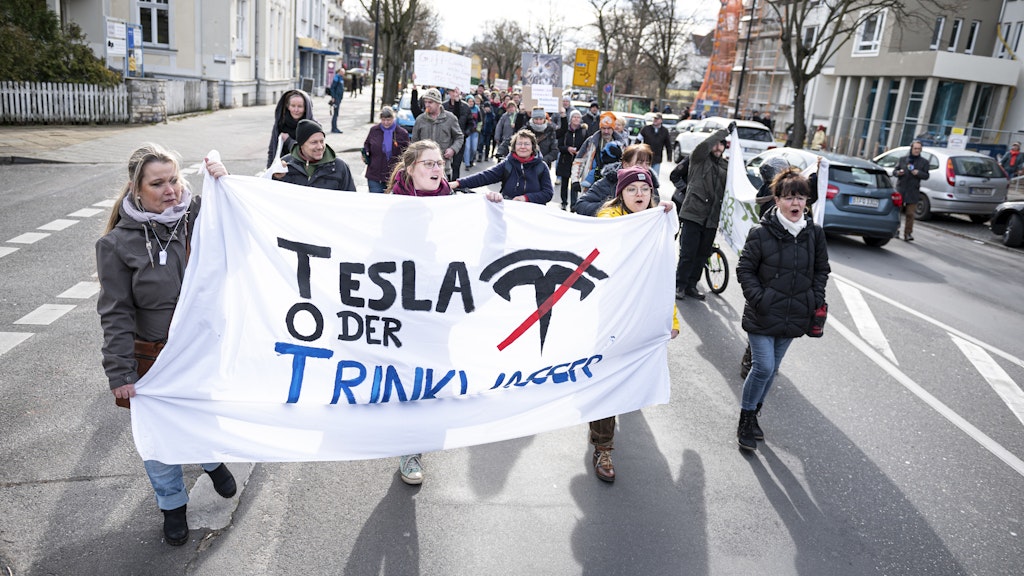 Demonstranten halten bei einem Protest gegen die geplante Tesla-Fabrik in Grünheide ein Banner mit der Aufschrift "Tesla oder Trinkwasser".