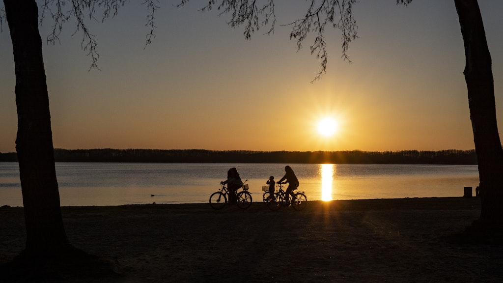 05.04.2020, Brandenburg, Rangsdorf: Menschen fahren mit ihren Fahrrädern bei Sonnenuntergang am Strand des Rangsdorfer See im brandenburgischen Landkreis Teltow-Fläming.