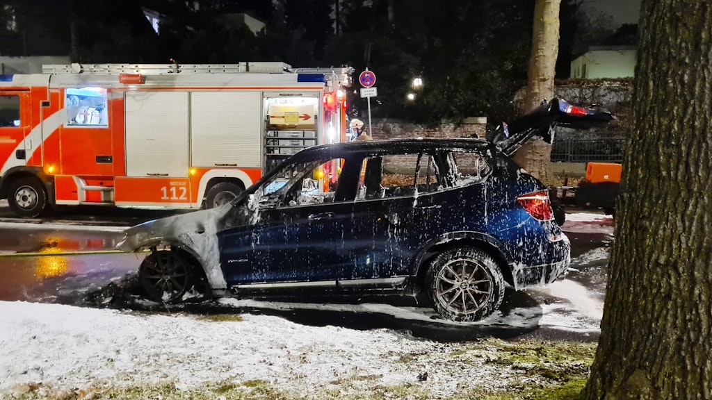 Das ausgebrannte Auto. Im Bildhintergrund: Ein Einsatzfahrzeug der Feuerwehr. 