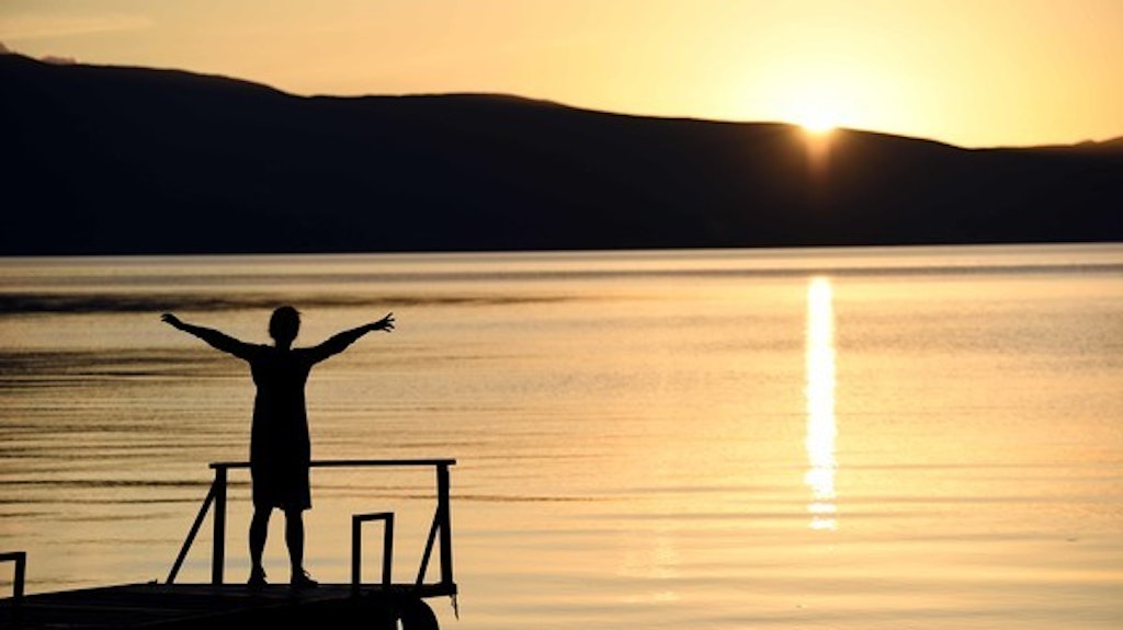 Eine Touristin steht bei Sonnenuntergang an einem See.