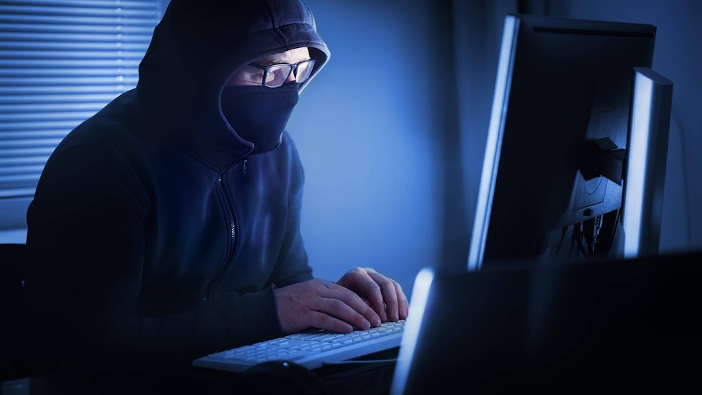 Ein maskierter Mann sitzt vor einem Computer (Symbolbild). 