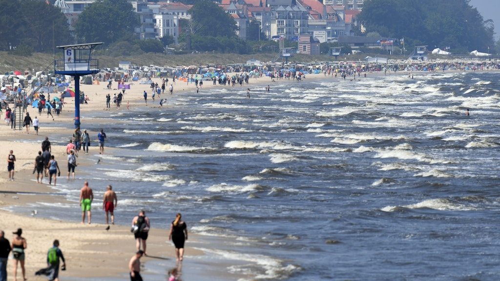 Touristen spazieren am Strand an der Ostsee auf der Insel Usedom entlang.