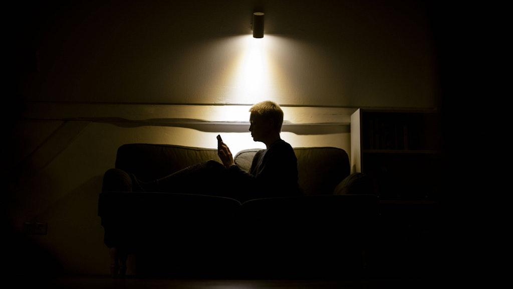 Eine Frau sitzt nachts auf der Couch und schaut in ein Smartphone.