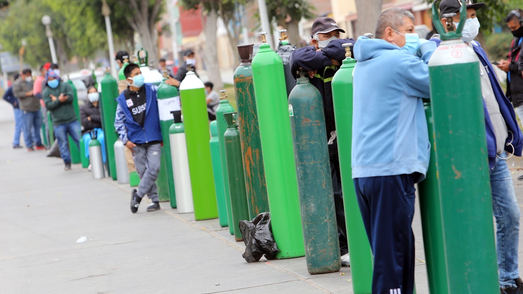 Peru, Lima: Menschen unterschiedlichen Alters mit Mundschutzmasken stehen Schlange neben ihren Sauerstoffflaschen vor einem Laden, in dem sie nachgefüllt werden.