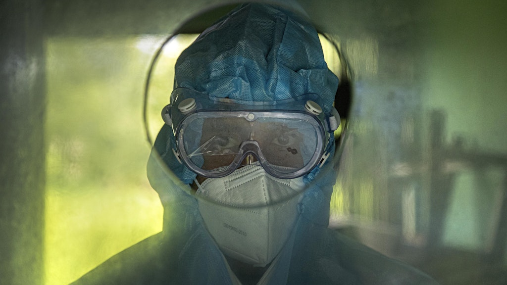Indien, Gauhati: Medizinisches Personal wartet hinter einer Glaswand darauf, Patienten Nasenabstriche zu entnehmen.