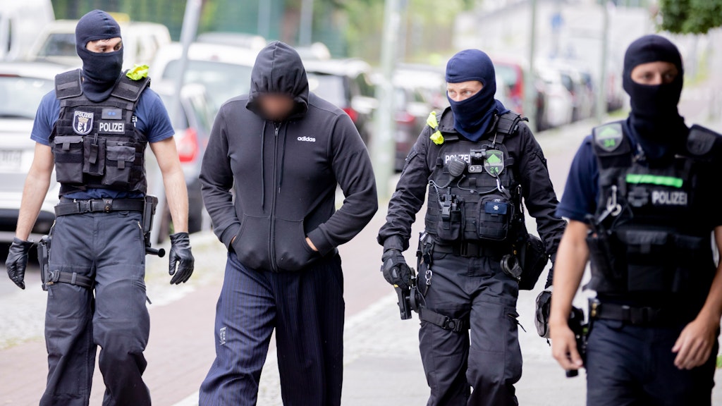 Polizisten mit Sturmhauben begleiten einen der Verdächtigen zu einem Einsatzwagen. Dort wurden seine Personalien kontrolliert. 