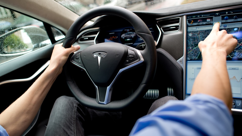 Ein Mann sitzt in einem Tesla auf dem Fahrersitz.