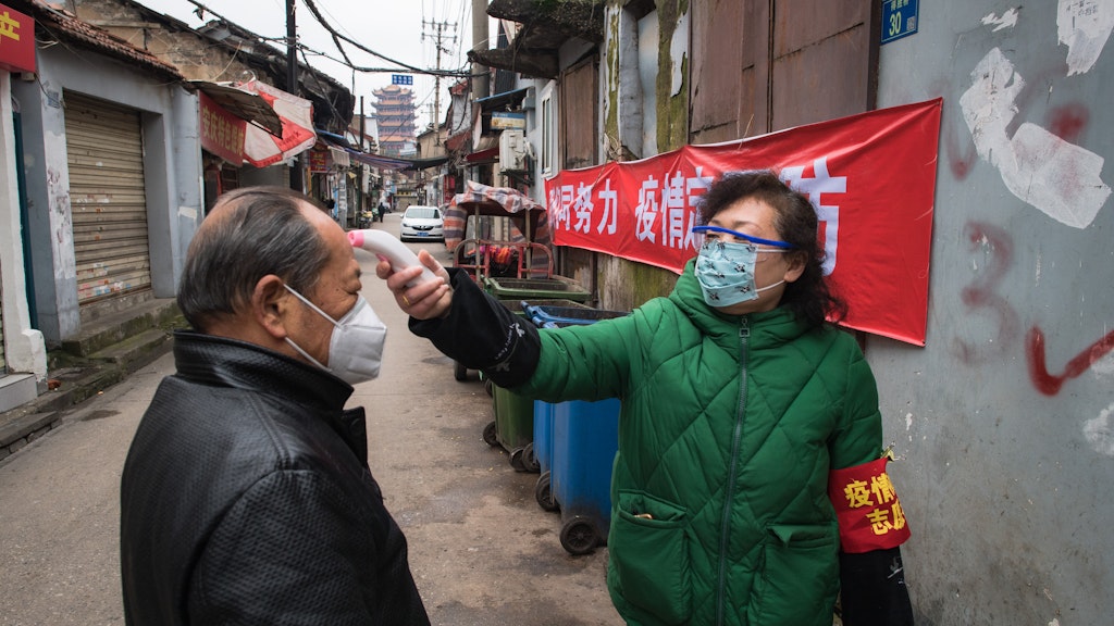 Wuhan: Eine Gemeindemitarbeiterin misst mit einem Fieberthermometer die Körpertemperatur eines Passanten. 