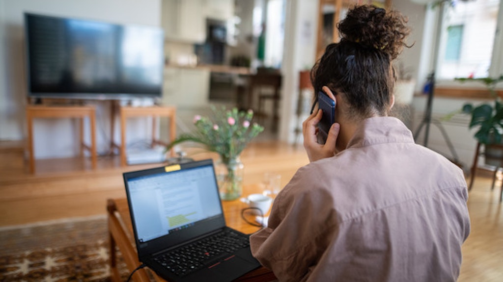 Eine Frau arbeitet im Homeoffice – in ihrem Wohnzimmer – und nimmt an einer Telefonkonferenz teil.