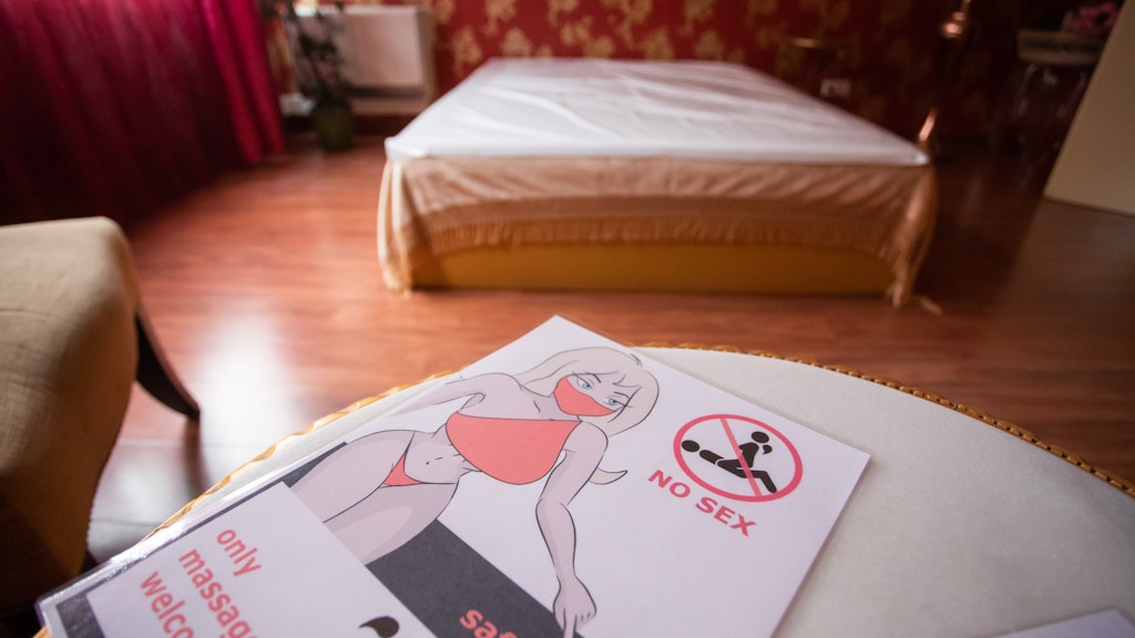 Ein Flyer mit der Aufschrift „No Sex, only massage welcome, safety first“ liegt auf einem Tisch in einem Arbeitszimmer eines Bordells. 