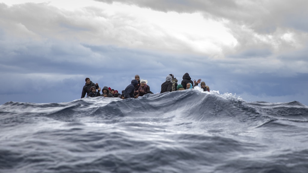 Männer aus Marokko und Bangladesch sitzen in einem überfüllten Holzboot im Mittelmeer vor der Küste Libyens.