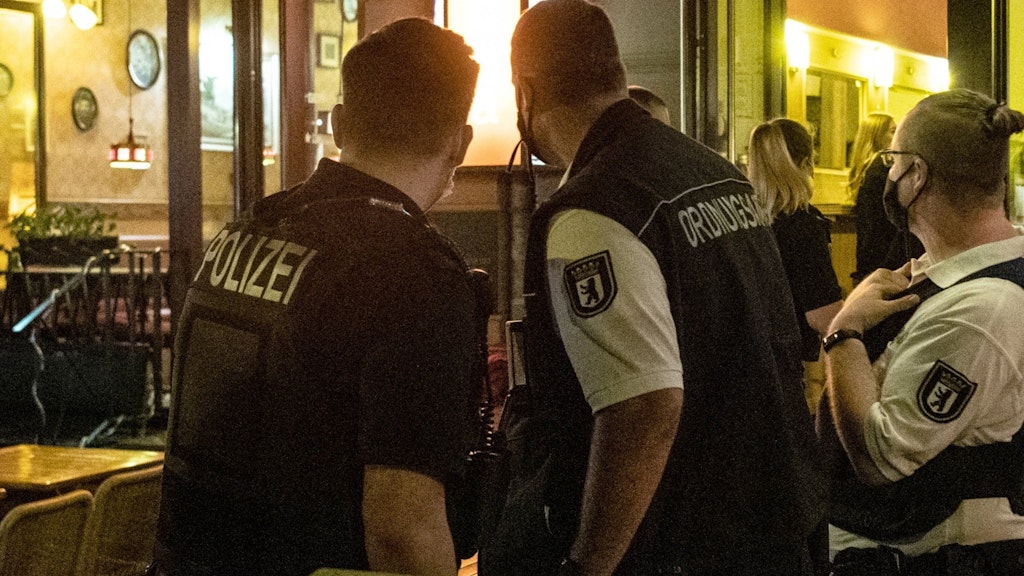 Ein Polizeibeamter und zwei Mitarbeiter des Ordnungsamtes stehen vor einem Lokal.
