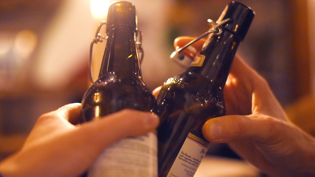 Zwei Personen stoßen in einer Kneipe mit Bier an. 