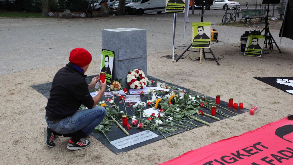 Ein Teilnehmer der Kundgebung stellt vor dem neu errichteten Denkmal auf dem Oranienplatz eine Kerze ab. 