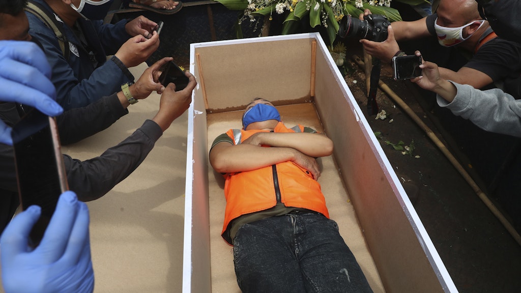 Jakarta: Ein Mann liegt in einem nachgemachten Sarg als Strafe für die Verletzung bestehender Corona-Regeln. 