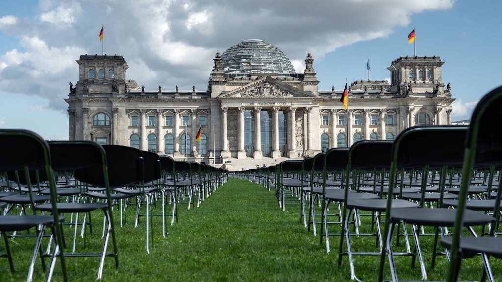 Wie ein stummes Publikum, die Augen auf das Parlament gerichtet, stehen die weißen und schwarzen Stühle da.