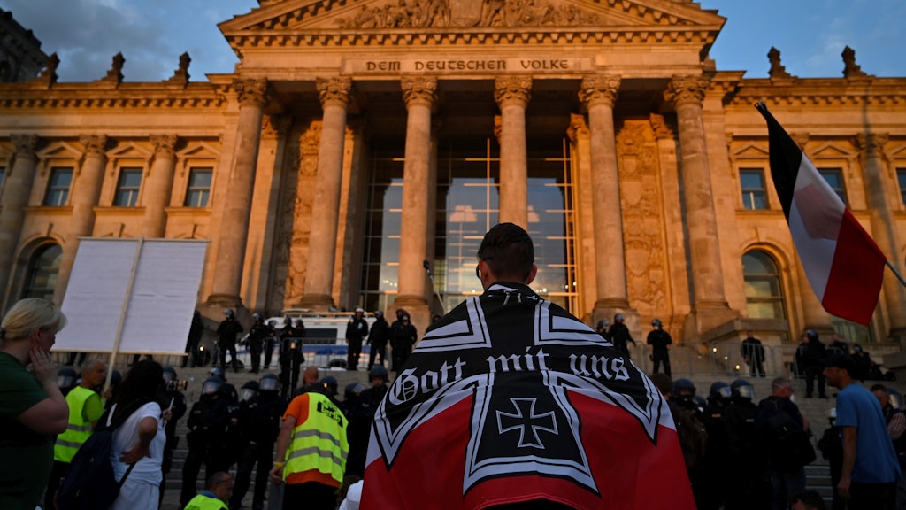 Ein Demonstrant steht in schwarz-weiß-rot-kaiserlicher deutscher Flagge vor dem Reichstagsgebäude.