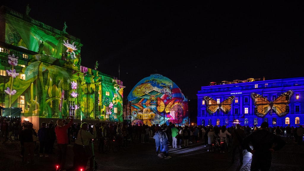 Zahlreiche Menschen stehen zum Auftakt des 17. Festival of Lights auf dem Bebelplatz. Dort sind alle Gebäude illuminiert. 