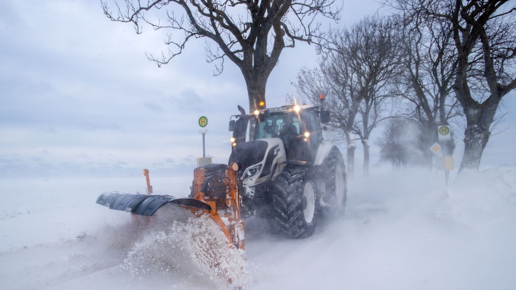 Ein Traktor mit einem Schneepflug räumt eine mit Schnee zugewehte Straße auf der Insel Rügen bei Putgarten.