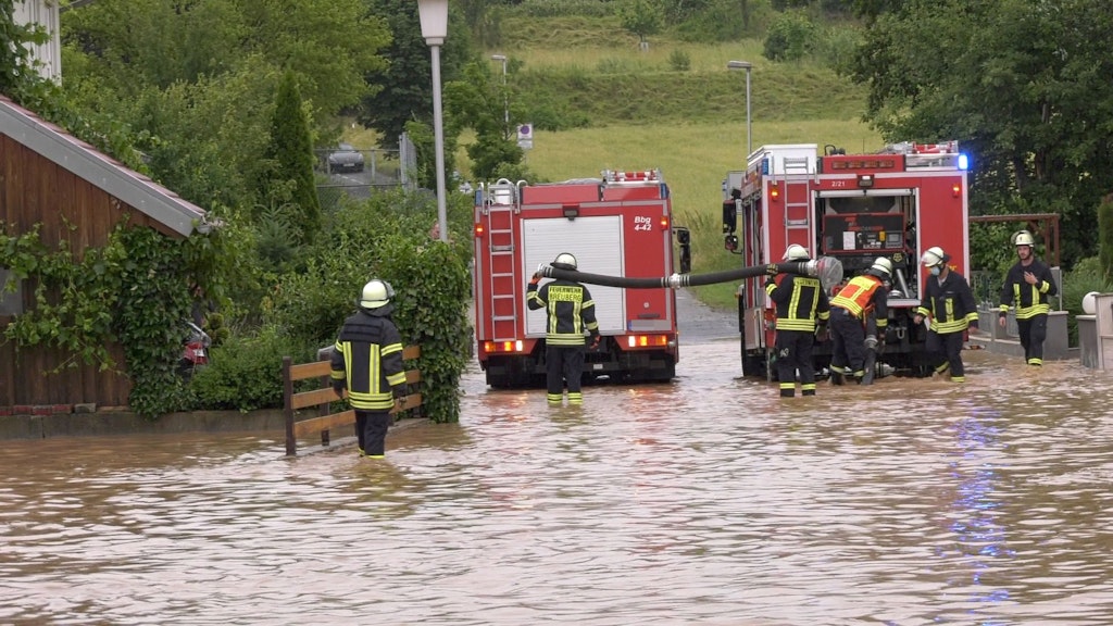 Hessen: Einsatzkräfte der Feuerwehr stehen in Breuberg (Odenwald) auf einer überfluteten Straße.