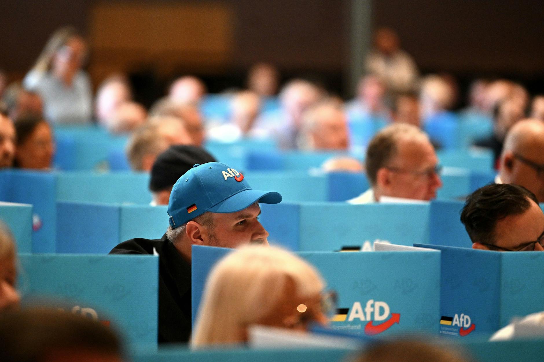 AfD members sit behind signs with the party logo during a state assembly.